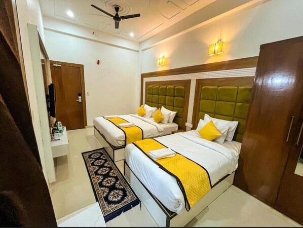 A hotel room with two beds, a ceiling fan, and a small table with a bottle. - Hotel Atlantiis Suites by Signature Stay (Agra)