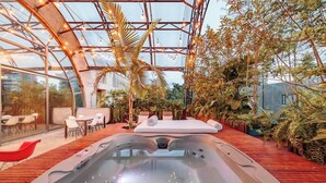 Area idromassaggio con soffitto in vetro, terrazza in legno e vegetazione circostante.