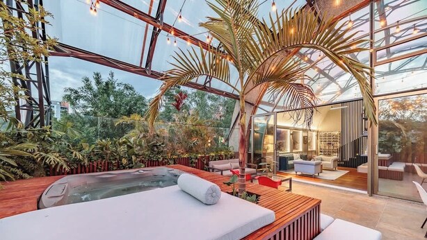 Un giardino interno moderno con idromassaggio, sedute in legno e un soggiorno vetrato.