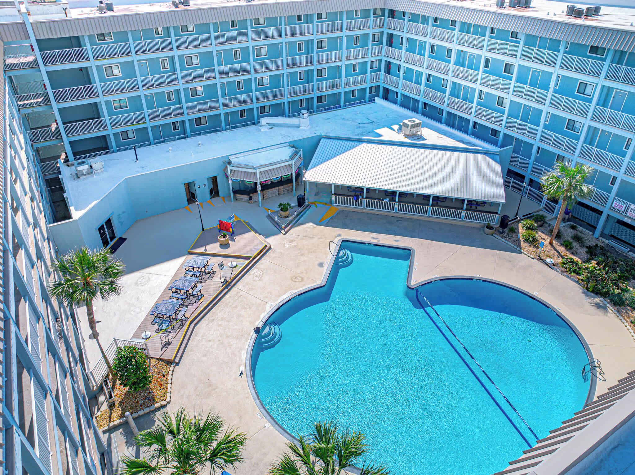 A multi-story hotel with a rooftop pool area, including lounge chairs and a covered seating area.