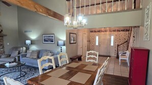Un salón espacioso con una gran mesa de comedor de madera, sillas blancas tapizadas y un techo alto con vigas a la vista.