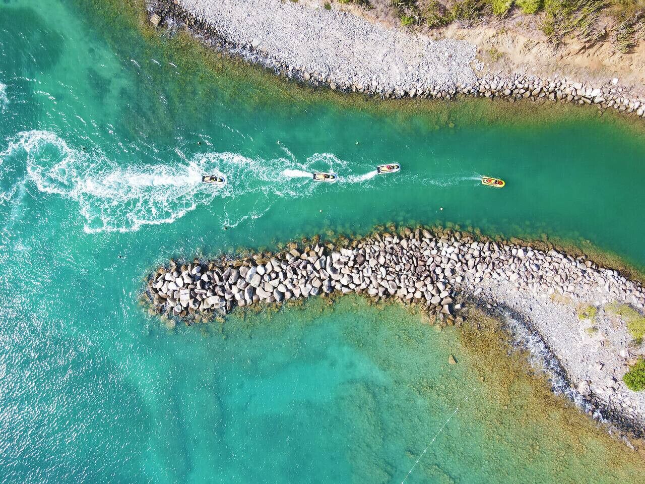 An aerial view of a coastal area with clear turquoise waters, a rocky breakwater, and kayaks in the water.
