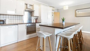 A modern kitchen with white cabinetry, a central island with bar stools, a dishwasher, and a stove. - Great 2-Bed Flat in Prime Location (Greater London)