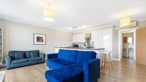 A modern living room with a blue sofa, a kitchen area, and a bathroom visible through an open door. - Great 2-Bed Flat in Prime Location (Greater London)