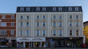 A multi-story building with ground-floor shops including a pharmacy and an optician. - Modern Flat in Prime Location (Greater London)