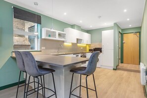 A modern kitchen with a central island, bar stools, and built-in cabinetry. - Spacious 2-Bed Flat with Outdoor Patio (Greater London)