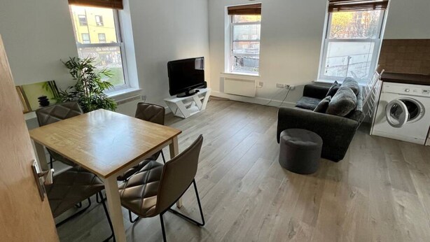 A modern living room with a wooden dining table, a sofa, a TV, and a washing machine. - Lovely 2-Bed Flat with Great Transport Links (Greater London)