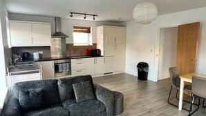 A modern living room with a grey sofa, a dining table with chairs, and a kitchen area with white cabinets and a microwave. - Lovely 2-Bed Flat with Great Transport Links (Greater London)