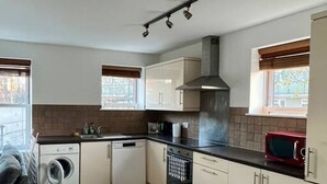 A compact kitchen with a washing machine, dishwasher, oven, and a microwave. - Lovely 2-Bed Flat with Great Transport Links (Greater London)