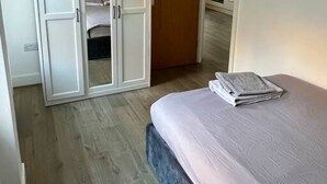 A bedroom with a bed, a wardrobe, and a view into the kitchen. - Lovely 2-Bed Flat with Great Transport Links (Greater London)