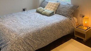 A bedroom with a bed, pillows, a nightstand with a lamp, and a window with a view of buildings. - Spacious Duplex near Clapham (Greater London)
