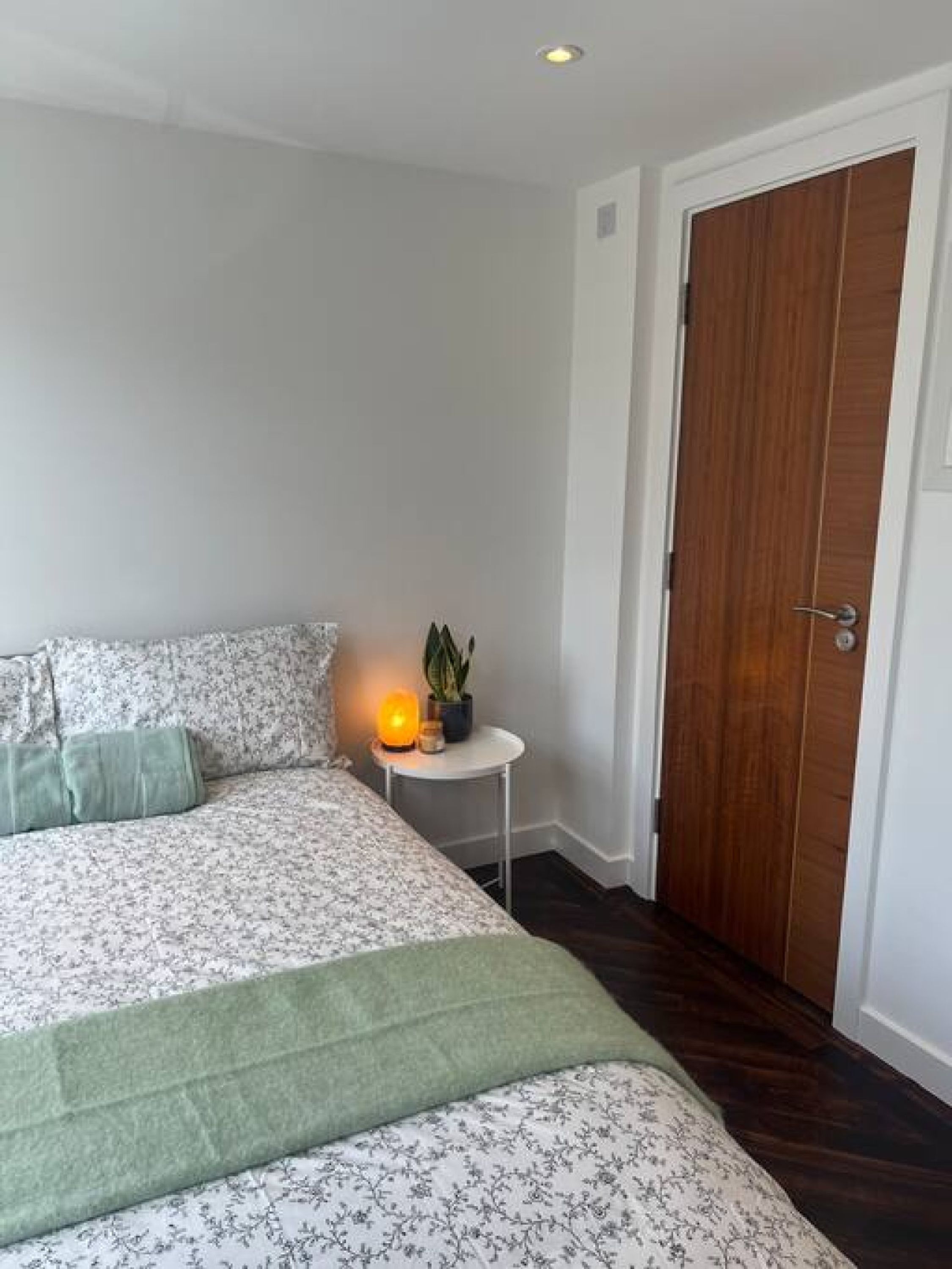 A bedroom with a bed, a bedside table with a lamp, and a wooden door.