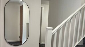 A staircase with white railings leading to a landing, a round mirror on the wall, and a carpeted floor. - Spacious Duplex near Clapham (Greater London)
