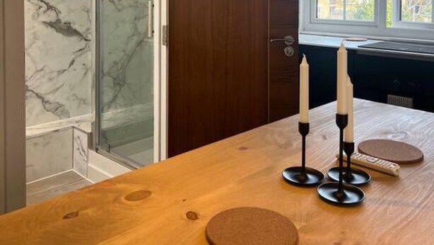 A modern kitchen with a wooden table, two candles, and a window with a view of buildings. - Spacious Duplex near Clapham (Greater London)