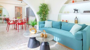 Ein modernes Wohnzimmer mit einem blaugrünen Sofa, roten Sesseln, einem runden Couchtisch und einer großen Pflanze.