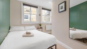 Une chambre à coucher avec un lit, une table de chevet ornée d’une plante, une fenêtre et un miroir.
