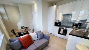 Un appartement moderne avec un canapé gris, une petite table à manger et un coin cuisine.