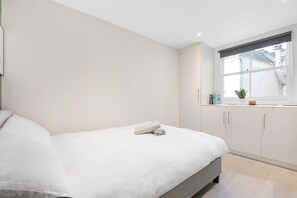 Een minimalistische slaapkamer met een bed, een raam met uitzicht en een klein kitchenette.