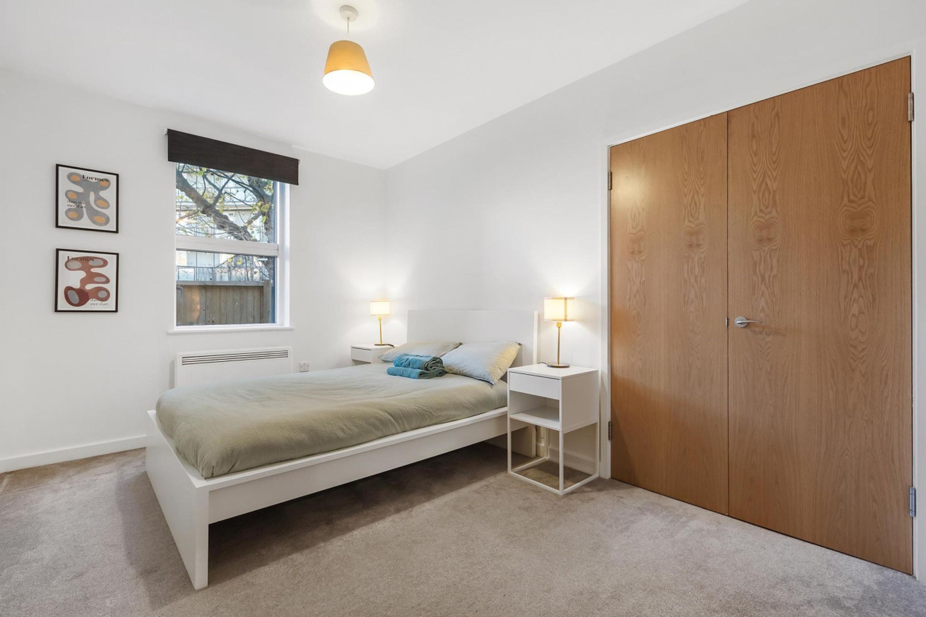 Een slaapkamer met een bed, nachtlampjes, een raam en een kledingkast.