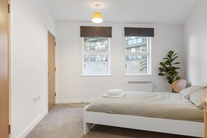A bedroom with a bed, two windows, a radiator, and a potted plant. - Garden Flat in Central London (Greater London)