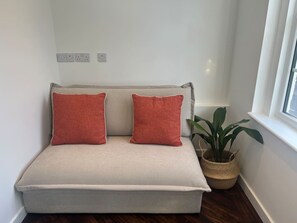 Ein Ecksofa mit zwei roten Kissen, ein gewebter Korb mit einer Pflanze und ein Fenster mit Blick.