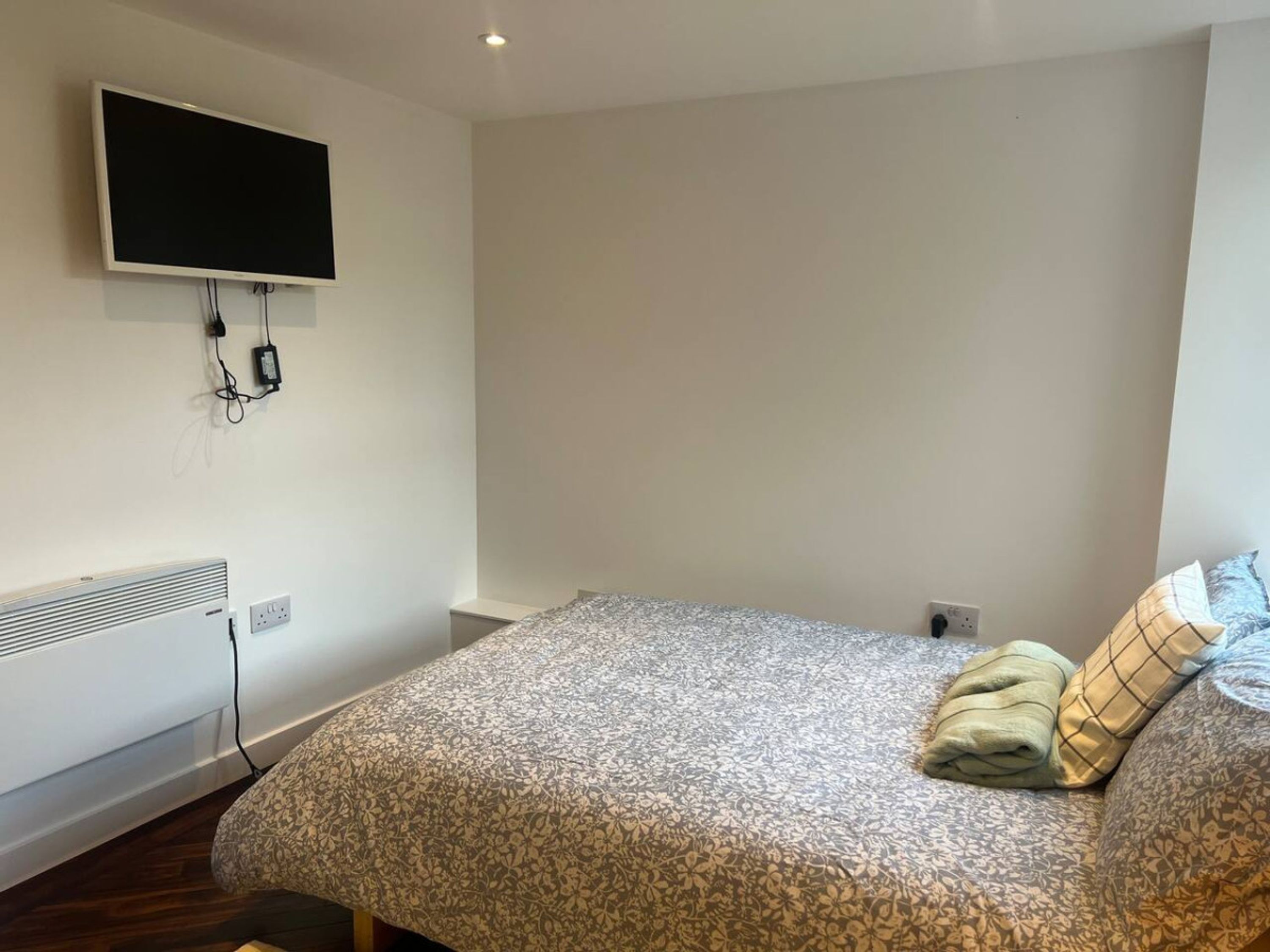 A bedroom with a bed, a flat-screen TV mounted on the wall, and a radiator.