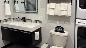 A modern bathroom with a white sink, black vanity, a toilet, and a towel rack. - Hungry Mosquito lodge 2-bedroom cabin 
near Nelson reservoir, relaxation awaits! (Saco)