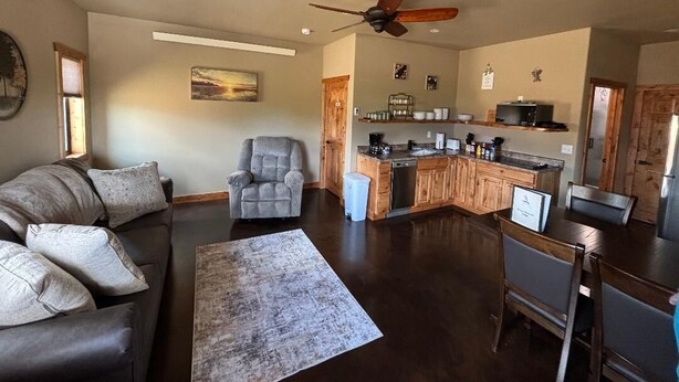 A spacious living area with a sofa, armchair, and a dining table. A kitchen with wooden cabinets and a built-in island is visible in the background. - Hungry Mosquito lodge 2-bedroom cabin 
near Nelson reservoir, relaxation awaits! (Saco)