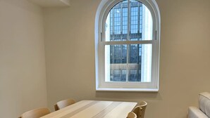 Un comedor con una mesa y sillas de madera, una ventana con vistas a edificios, y un suelo de tonos claros.