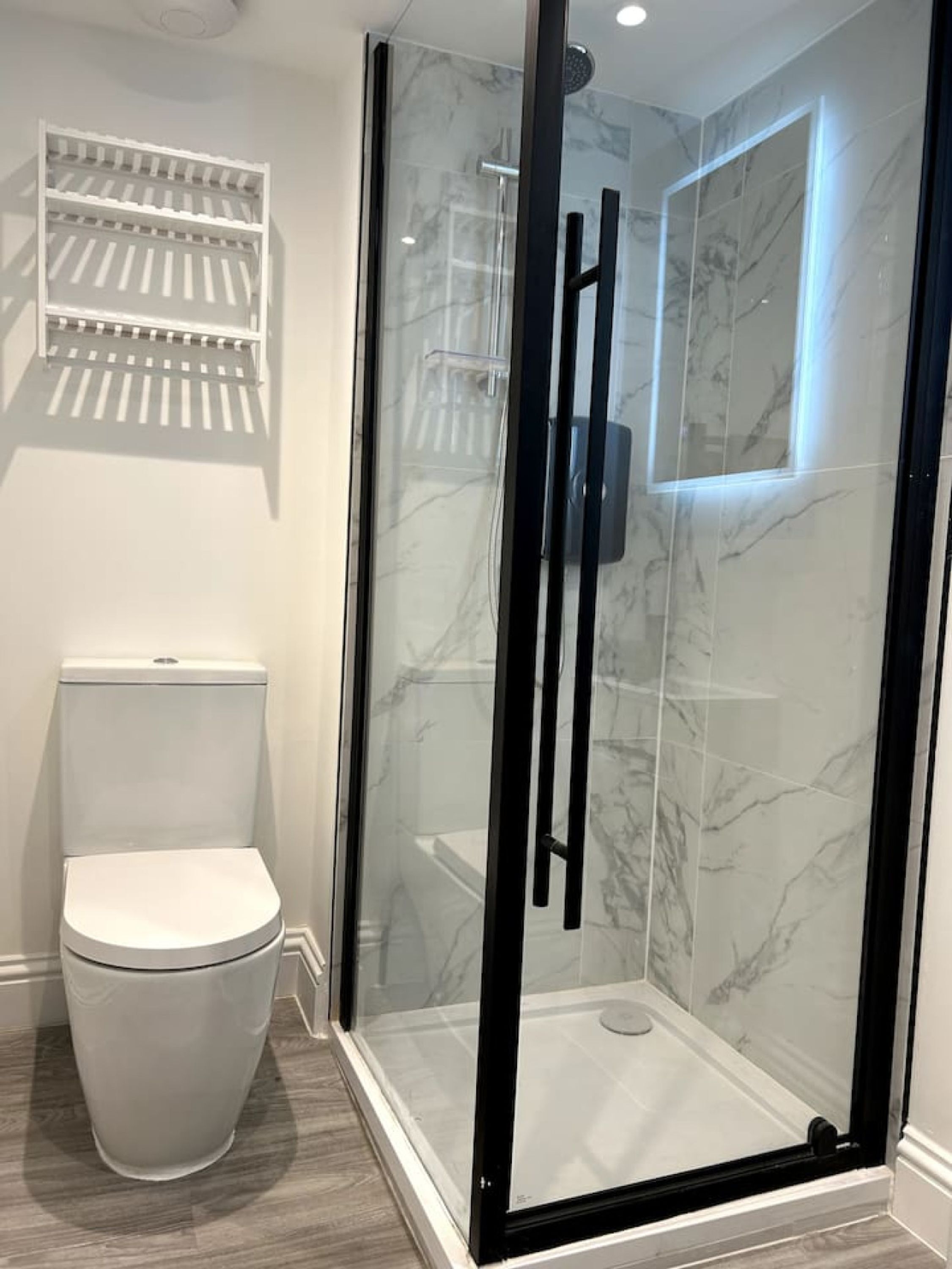 A modern bathroom with a glass-enclosed shower, a white toilet, and a marble-tiled shower wall.