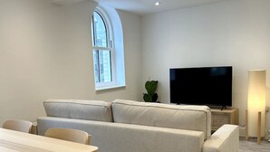 Una sala moderna con un sofá, un televisor, una mesa de comedor y un ventanal.