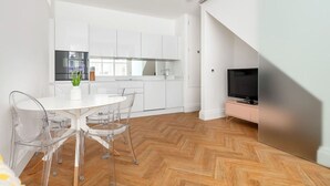 A modern kitchen with white cabinets, a dining table with clear chairs, and a TV on a pink stand. - Charming Mews House in Kensington (Greater London)