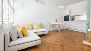 A modern apartment with a white sofa, a dining table, and a kitchen area. - Charming Mews House in Kensington (Greater London)
