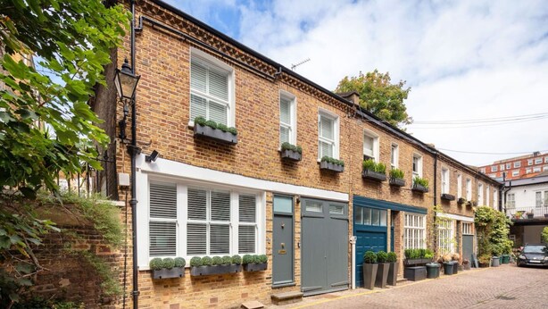 A row of terraced houses with brick facades, white window frames, and small balconies with plants. - Charming Mews House in Kensington (Greater London)