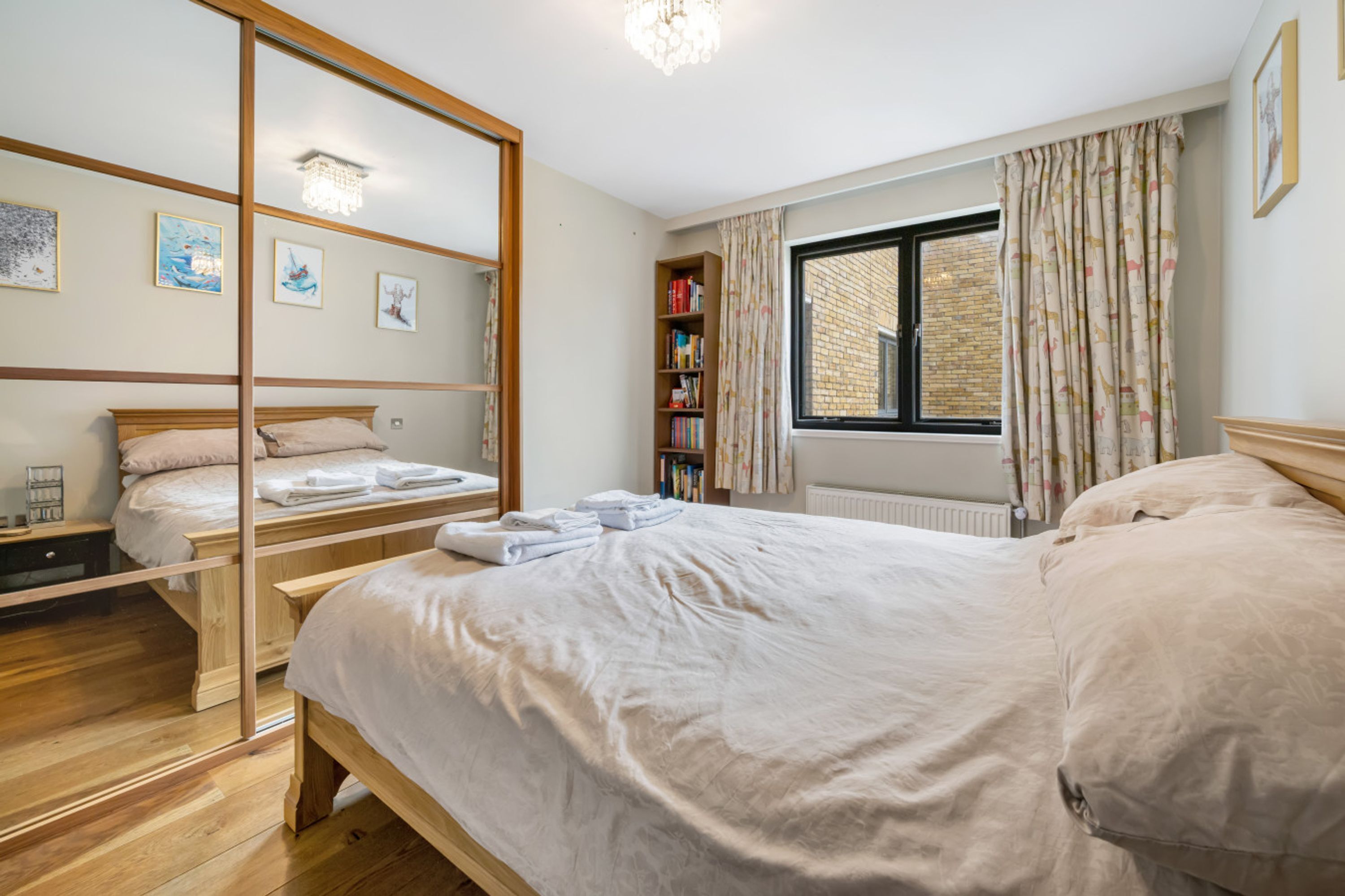 A bedroom with a large bed, a wardrobe with a mirror, a bookshelf, and a window with curtains.