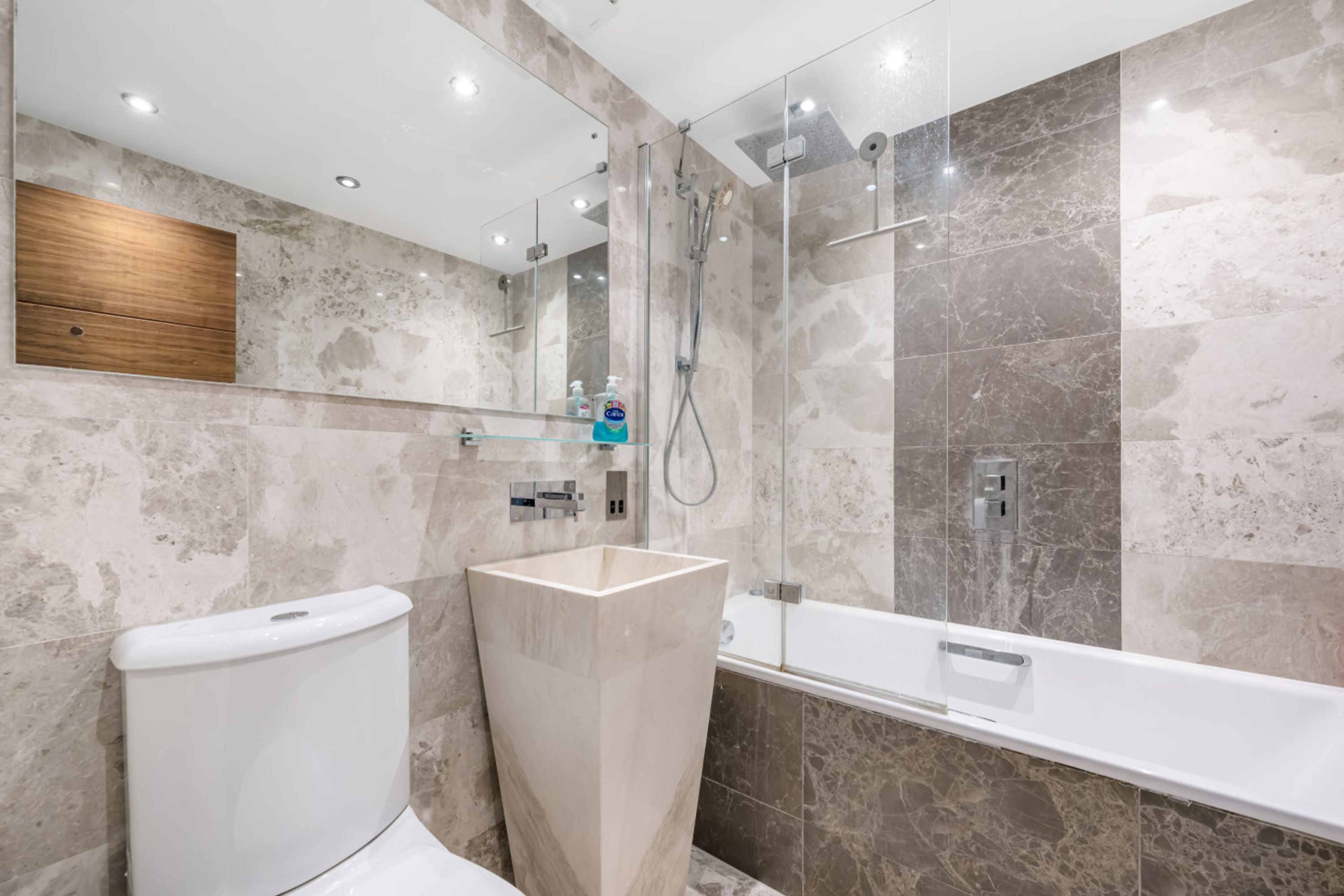 A modern bathroom with a toilet, a large rectangular sink, a glass shower enclosure, and a bathtub.