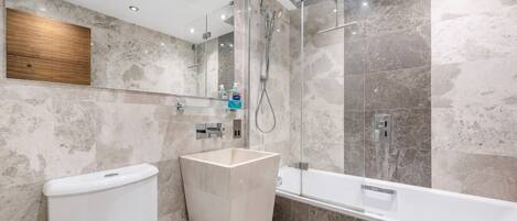 A modern bathroom with a toilet, a large rectangular sink, a glass shower enclosure, and a bathtub.