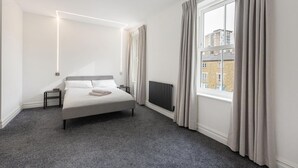 Ein modernes Schlafzimmer mit einem großen Bett, einem Heizkörper, einem Fenster mit Vorhängen und Blick auf Gebäude.