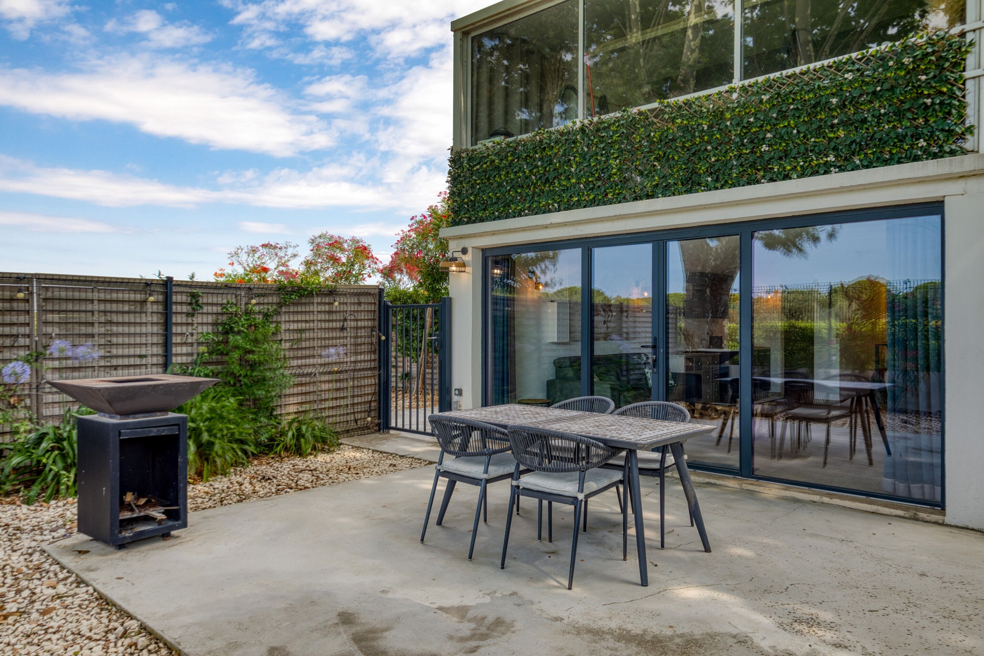 Une terrasse extérieure moderne, dotée d’une table et de chaises, d’un foyer et d’un espace repas fermé par des parois de verre.