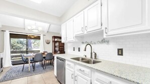 A modern kitchen with white cabinets, a granite countertop, and a large window offering a view of the outdoors. - Seascape Golf Villas 10G (Miramar Beach)