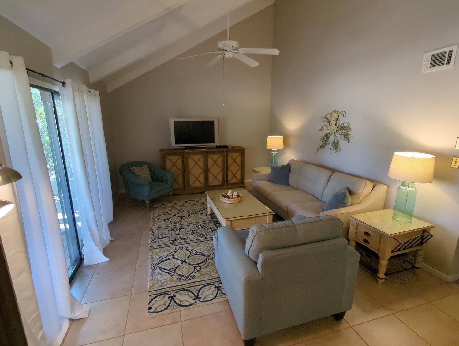 A living room with a sofa, armchair, TV, and decorative lamps.