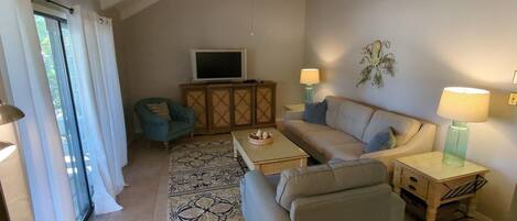 A living room with a sofa, armchair, TV, and decorative lamps.