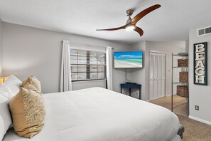 Ein Schlafzimmer mit Bett, Deckenventilator, Fernseher und Blick auf den Strand.