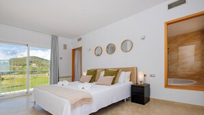 Un dormitorio con una cama grande, una mesita de noche, un ventanal con vistas a la vegetación y una bañera con marco de madera.