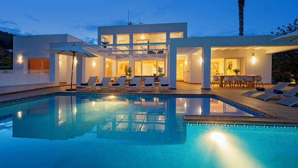 Una casa moderna con piscina, tumbonas y zona de comedor.