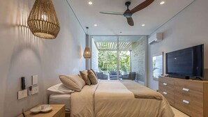 Ein modernes Schlafzimmer mit einem großen Bett, einem Fernseher, einem Deckenventilator und Blick ins Freie.