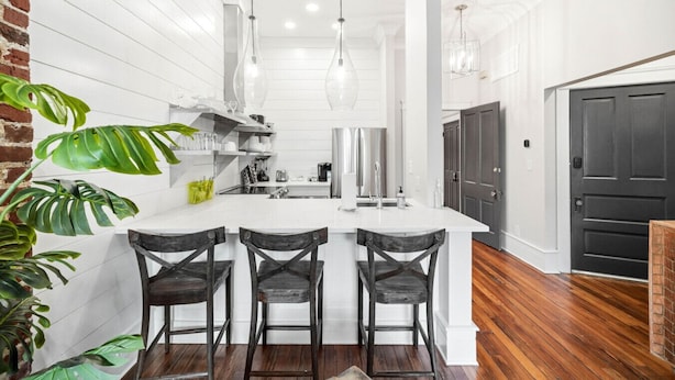 A modern kitchen with white cabinetry, a central island with bar stools, and a brick accent wall. - Old City Loft | Knoxville (Knoxville)