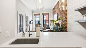 A modern kitchen with a large island, a brick accent wall, and pendant lighting. - Old City Loft | Knoxville (Knoxville)