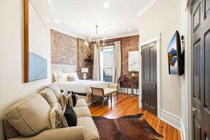 A bedroom with a large bed, a wooden floor, a brick wall, a chandelier, and a TV mounted on the wall. - The Luxe Loft | Knoxville (Knoxville)