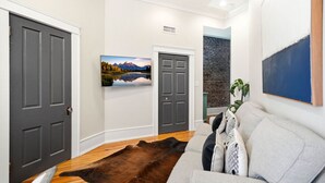 A living room with a large leather rug, a grey sofa, and a mounted painting of a mountain landscape.